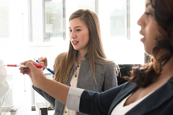 Eine Lehrperson zeigt einem Erwachsenen Inhalte auf einem Whiteboard.